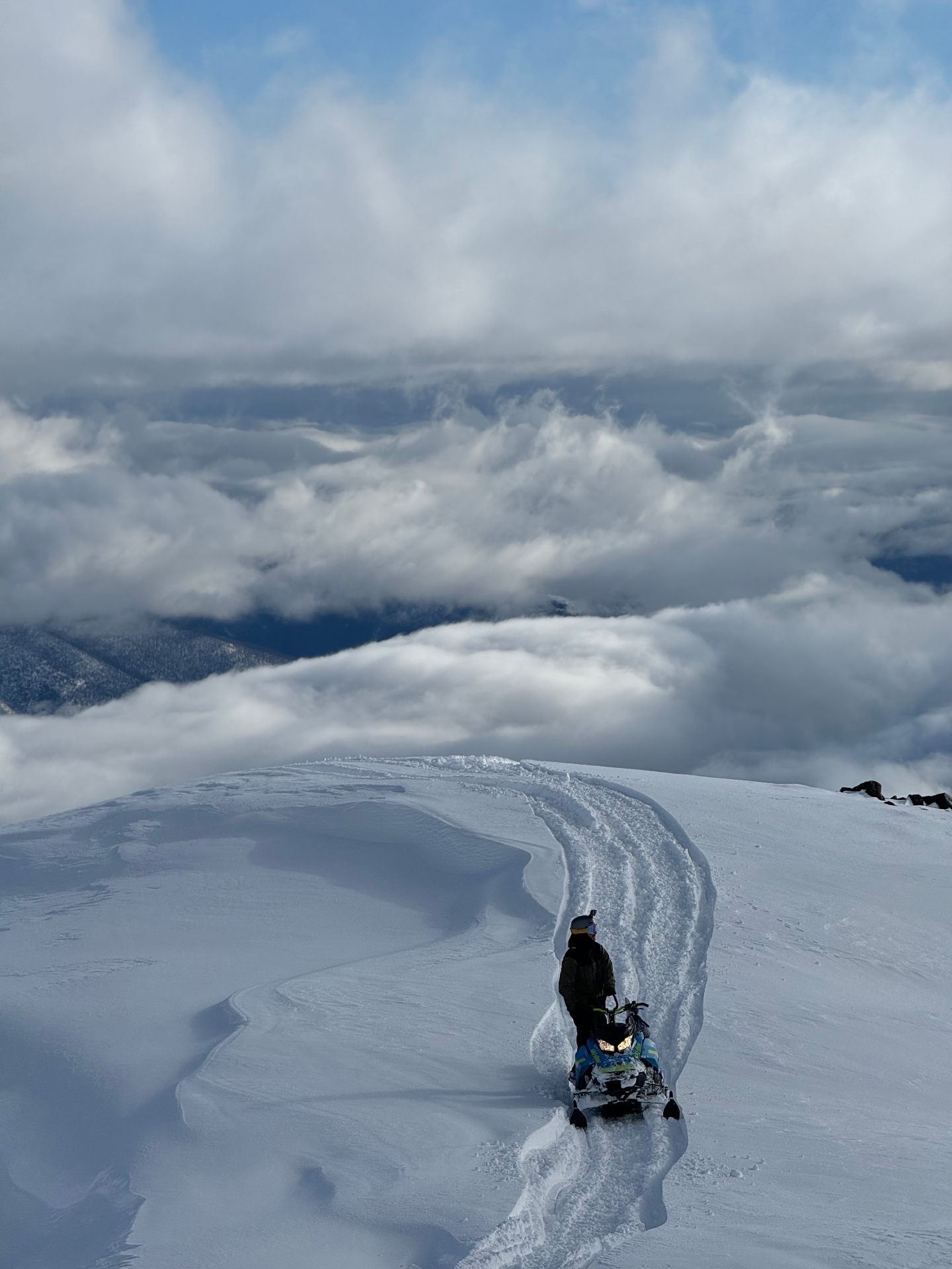 Moto de nieve dejando huella en la cumbre sobre las nubes