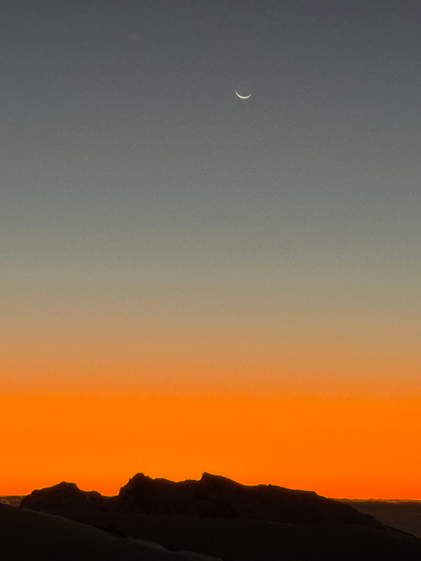 Luna creciente sobre cumbre andina al atardecer naranja