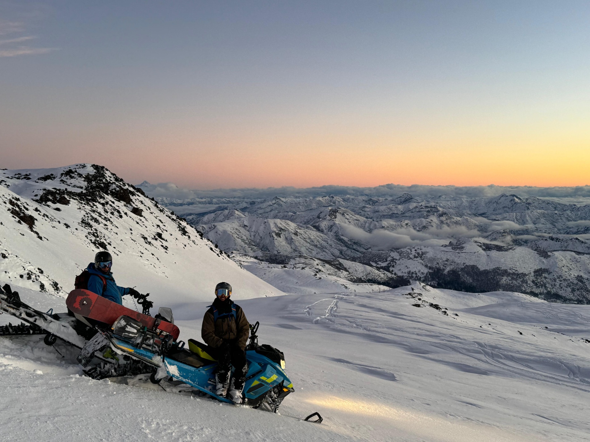 Riders con moto de nieve Ski-Doo Summit al atardecer sobre la cordillera