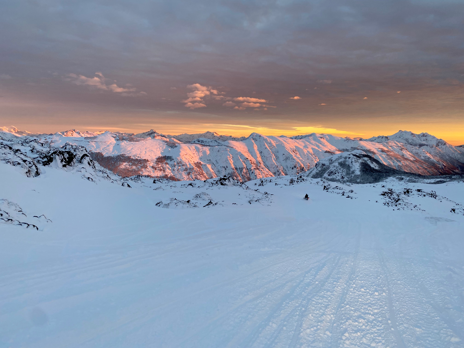 Atardecer sobre la cordillera nevada con moto de nieve a lo lejos